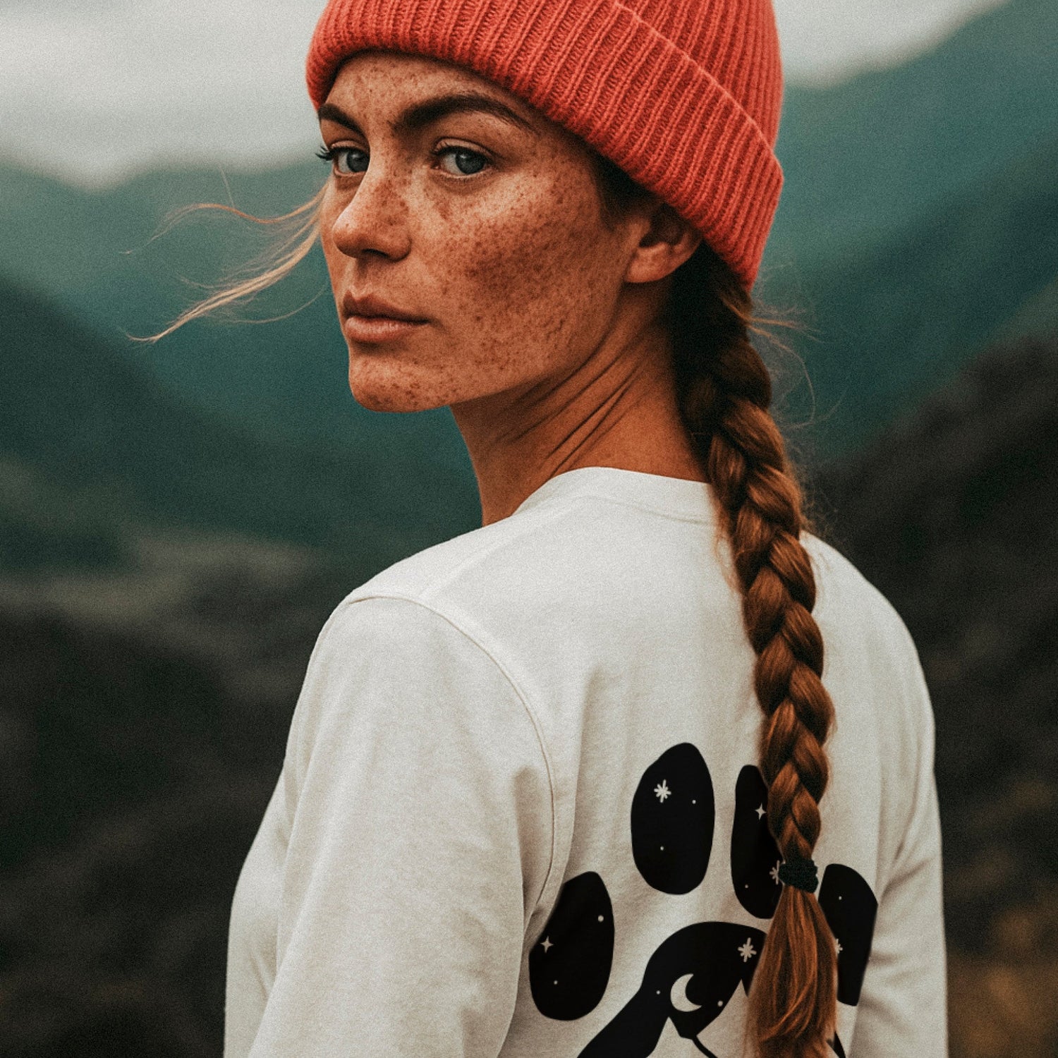 Junge Frau mit gepflochtenen Haaren und Beanie trägt ein Bio-Baumwoll Longsleeve mit Pfotenmotiv. Adventure Together steht für gemeinsame Abenteuer mit ihrem Hund.